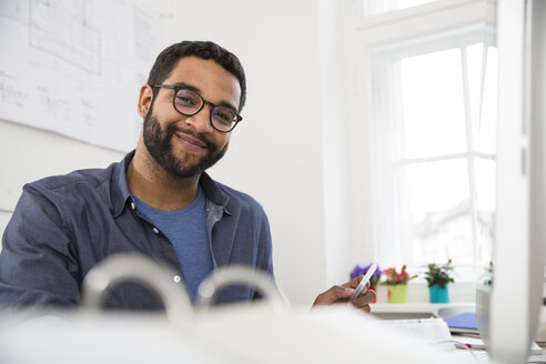 Portrait of smiling man at desk in office - FKF001868