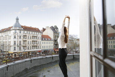 Junge Frau streckt sich auf der Dachterrasse - FKF001871