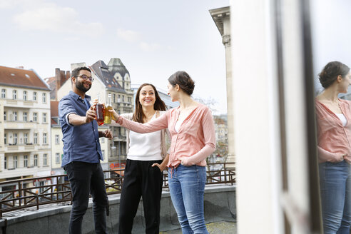 Mann und zwei Frauen stoßen auf der Dachterrasse mit Flaschen an - FKF001872