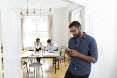 Man in office using tablet with colleagues in background - FKF001878