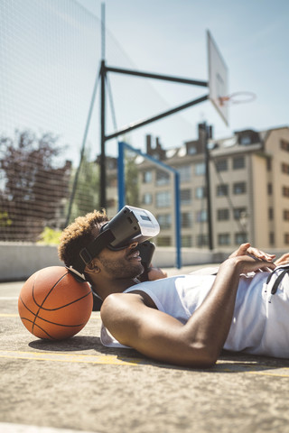 Junges Paar, das eine Virtual-Reality-Brille benutzt und den Kopf auf einem Basketball ablegt, lizenzfreies Stockfoto