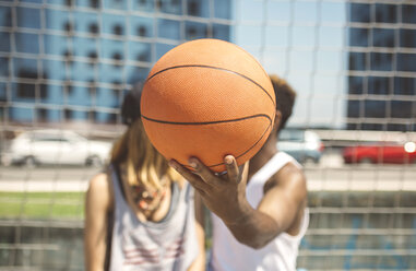 Young couple hiding faces behind basketball - DAPF000176