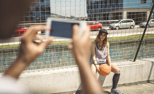 Junger Mann, der eine junge Frau auf dem Basketballplatz fotografiert - DAPF000177