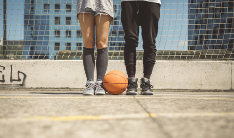 Junger Mann und Frau stehen auf dem Basketballfeld mit zwischen den Füßen, lizenzfreies Stockfoto