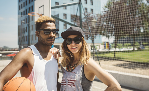 Junges Paar steht auf einem Basketballfeld und schaut in die Kamera, lizenzfreies Stockfoto