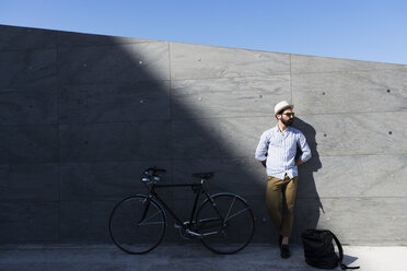 Junger Mann mit Fahrrad und Rucksack lehnt an der Wand - FMOF000005