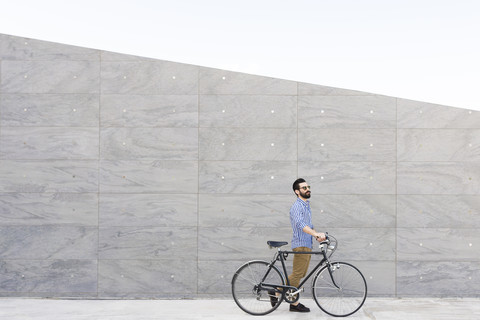 Junger Mann mit Fahrrad vor einer grauen Wand, lizenzfreies Stockfoto