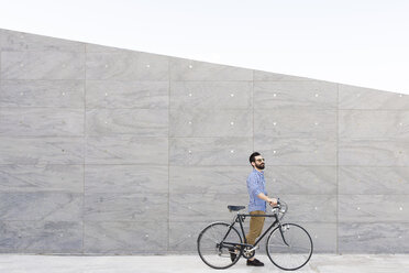 Junger Mann mit Fahrrad vor einer grauen Wand - FMOF000007