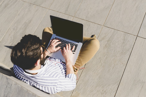 Junger Mann sitzt auf dem Boden und benutzt einen Laptop, lizenzfreies Stockfoto
