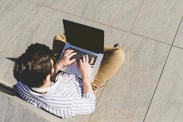 Junger Mann sitzt auf dem Boden und benutzt einen Laptop - FMOF000017