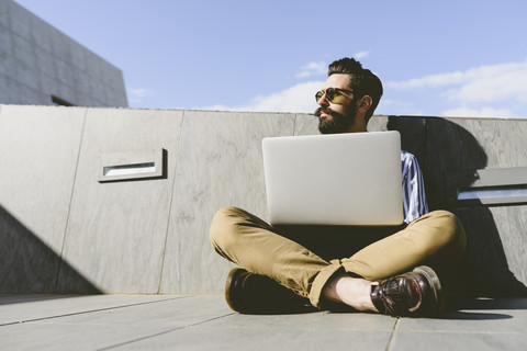 Young man sitting on the ground with laptop stock photo