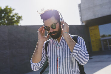 Bärtiger junger Mann mit Sonnenbrille hört Musik mit Kopfhörern - FMOF000020