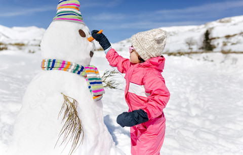 Spanien, Asturien, Mädchen baut einen Schneemann im Winter, lizenzfreies Stockfoto