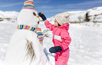 Spanien, Asturien, Mädchen baut einen Schneemann im Winter - MGOF001971