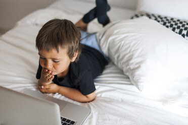 Lächelnder kleiner Junge auf dem Bett liegend mit Laptop - VABF000580
