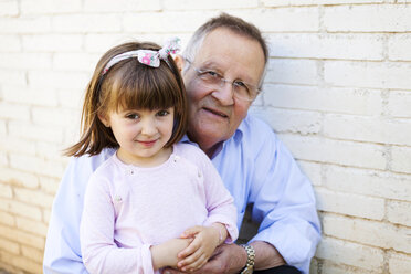 Portrait of grandfather with his little granddaughter in front of white brick wall - VABF000583