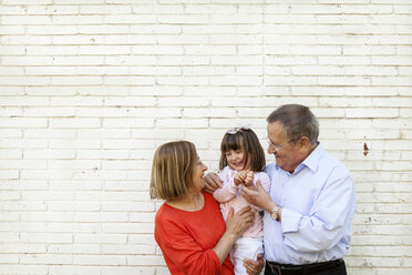 Großeltern mit ihrer Enkelin vor einer weißen Backsteinmauer - VABF000586