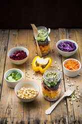 Zwei Gläser Regenbogensalat mit Kichererbsen, Sprossen und verschiedenen Gemüsesorten und Schalen mit Zutaten - LVF004973