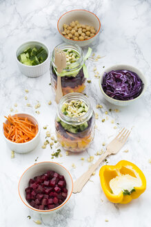 Zwei Gläser Regenbogensalat mit Kichererbsen, Sprossen und verschiedenen Gemüsesorten und Schalen mit Zutaten - LVF004978