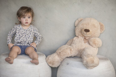 Ernstes kleines Mädchen und Teddybär auf Hocker sitzend - ZEF008727