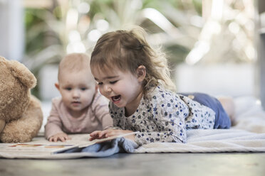 Zwei Baby-Mädchen liegen auf einer Decke auf dem Boden und betrachten ein Buch - ZEF008729