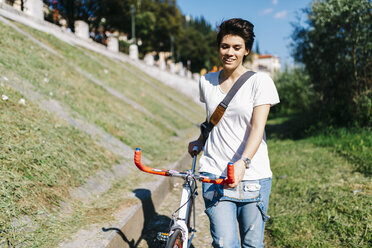 Smiling young woman pushing bicycle - GIOF001219