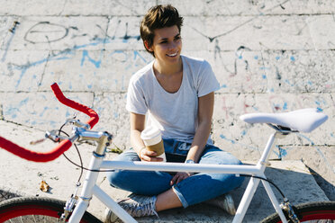 Smiling young woman with bicycle and coffee to go - GIOF001225