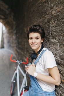 Porträt einer lächelnden jungen Frau mit Fahrrad an einer Steinmauer - GIOF001247