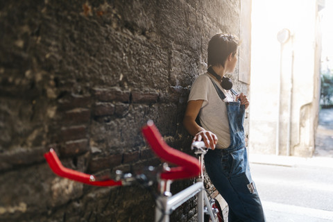 Junge Frau mit Fahrrad an eine Steinmauer gelehnt, lizenzfreies Stockfoto
