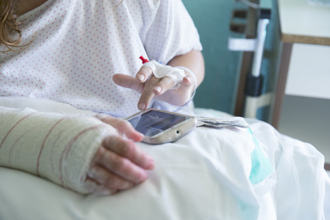 Frau im Krankenhaus, operierte Hand, benutzt Handy, linke Hand, lizenzfreies Stockfoto