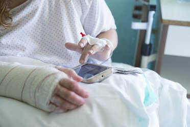 Frau im Krankenhaus, operierte Hand, benutzt Handy, linke Hand - ERLF000178