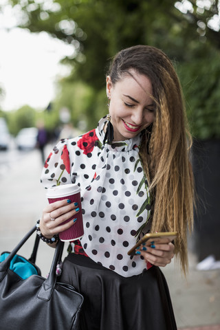 Portrait of smiling woman with coffee to go looking at her smartphone stock photo