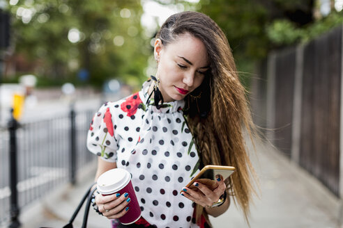 Portrait of young woman with coffee to go looking at her smartphone - MAUF000663