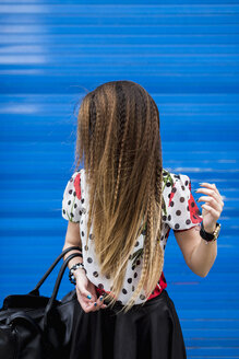 Braided hair of stilished young woman in front of blue roller shutter - MAUF000665