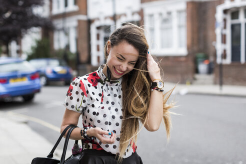 UK, London, portrait of smiling young woman with blowing hair - MAUF000666