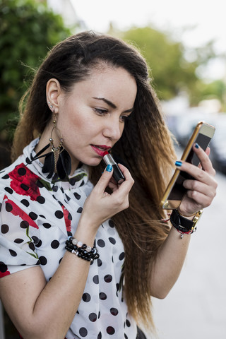 UK, London, young woman applying lipstick with the aid of her smartphone stock photo