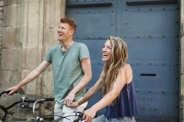 Portrait of laughing woman with bicycle holding hand with her boyfriend in the background - VABF000592