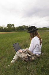 Frau sitzt auf einer Wiese und benutzt einen Laptop - BOYF000425
