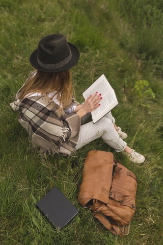 Junge Frau sitzt auf einer Wiese und liest ein Buch, lizenzfreies Stockfoto