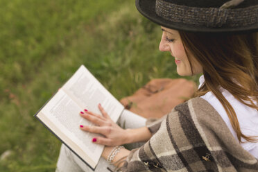Junge Frau sitzt auf einer Wiese und liest ein Buch - BOYF000437
