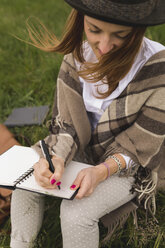 Junge Frau sitzt auf einer Wiese und schreibt etwas in ihr Notizbuch - BOYF000439