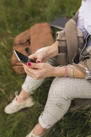 Junge Frau auf einer Wiese, die mit Kopfhörern und Smartphone Musik hört, lizenzfreies Stockfoto