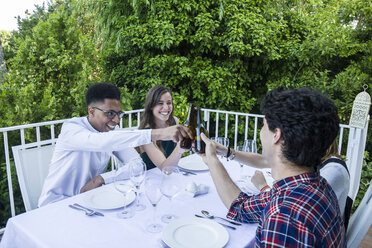 Freunde stoßen bei einem sommerlichen Abendessen mit Bierflaschen an - ABZF000722