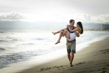 Mann trägt seine Freundin am Strand - ABAF002053