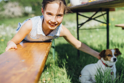 Porträt eines lächelnden Mädchens mit Hund auf einer Holzbank liegend - MJF001944