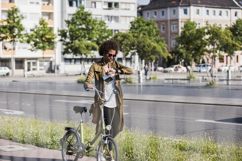 Young woman with with bicycle checking the time - UUF007733