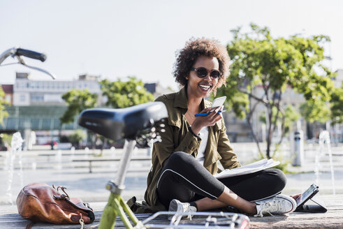 Portrait of young woman sitting on a bench using smartphone and digital tablet - UUF007740