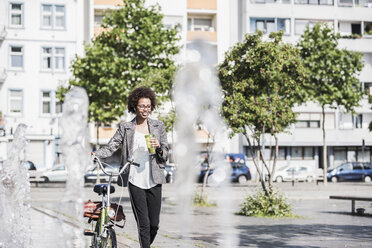 Porträt einer lächelnden Frau mit Fahrrad, die mit Kopfhörern Musik hört - UUF007750