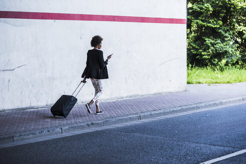 Businesswoman with baggage and smartphone walking down the street - UUF007757