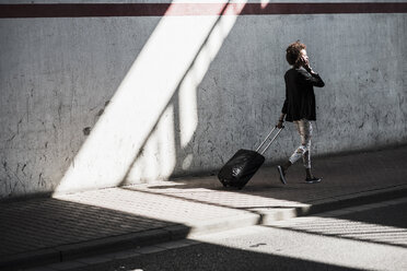 Walking businesswoman with baggage telephoning with smartphone - UUF007758